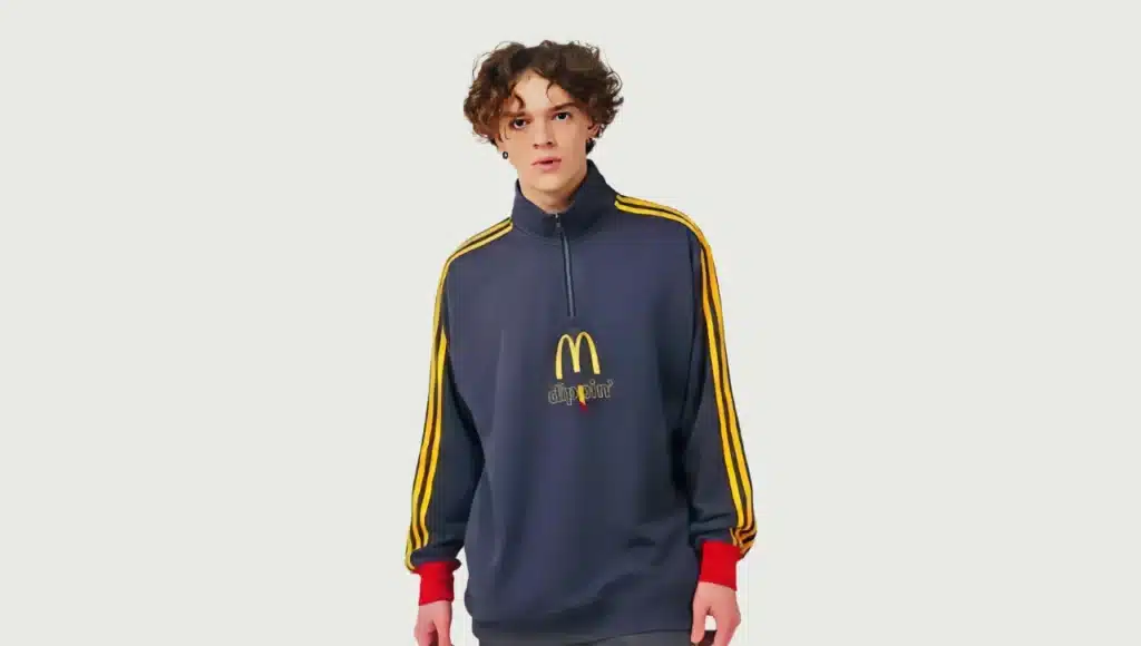 A person wearing a dark blue half-zip sweatshirt featuring yellow stripes on the sleeves and a McDonald's-inspired logo on the front, along with red cuffs.