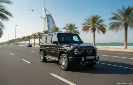 A black Mercedes-Benz G-Class SUV driving on a wide road lined with palm trees, with the Burj Al Arab in the background against a clear blue sky in Dubai, UAE.