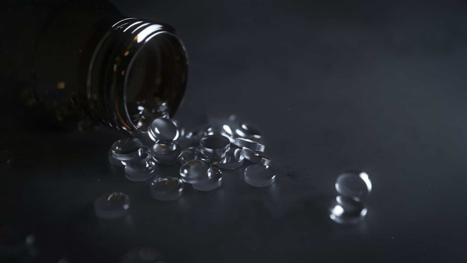A dark glass bottle tipped over with clear gel capsules spilling out onto a dark surface.