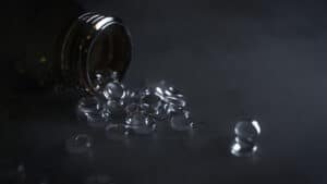 A dark glass bottle tipped over with clear gel capsules spilling out onto a dark surface.