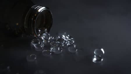A dark glass bottle tipped over with clear gel capsules spilling out onto a dark surface.