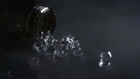 A dark glass bottle tipped over with clear gel capsules spilling out onto a dark surface.