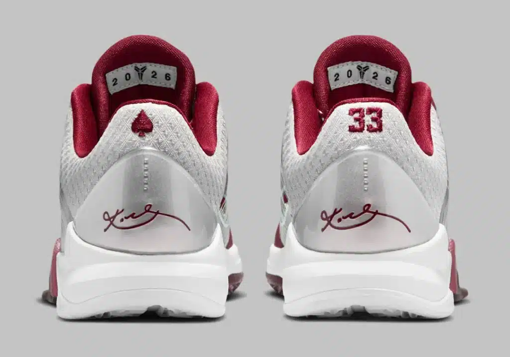 Back view of a pair of white and burgundy athletic shoes with a spade symbol above the heel and the number 33 embroidered on each heel. Inside the shoes, '2026' is visible on the heel lining, and a signature is printed on the heel counter.