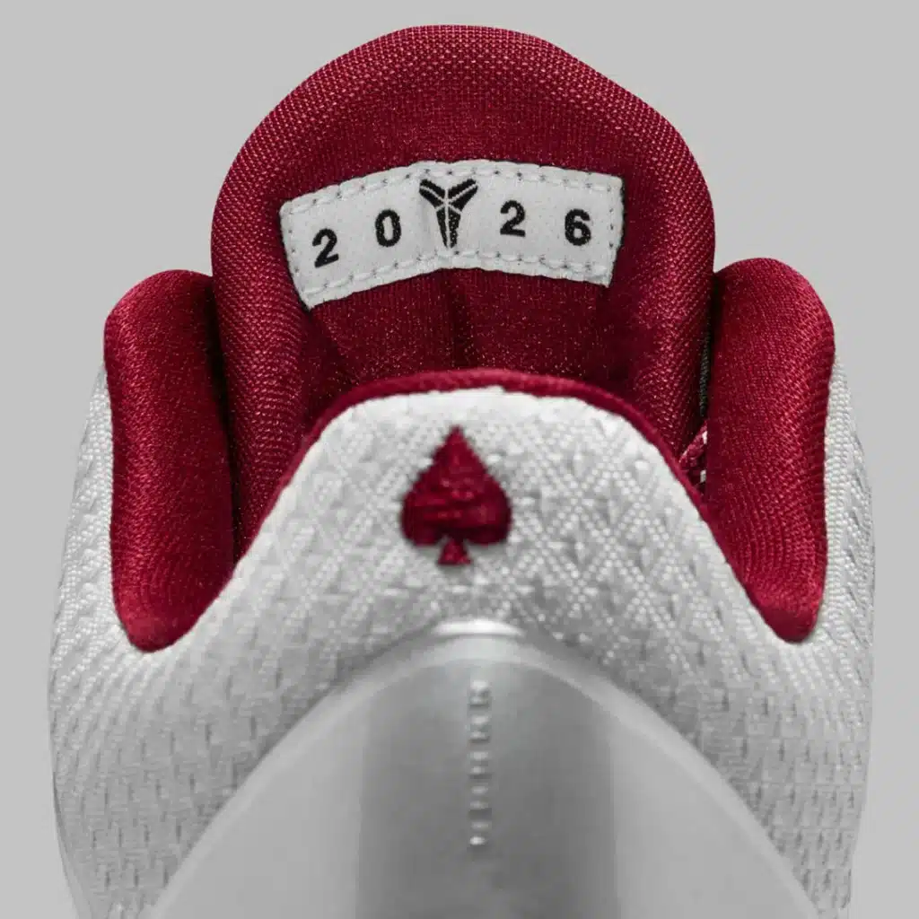 Close-up view of a red and white sneaker tongue featuring a stylized logo, the numbers 20 and 26, and a small embroidered spade symbol.