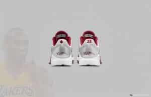 Back view of a pair of sneakers with white and burgundy colors, featuring a signature and a number 33 on the heels. A faded image of a basketball player in a Lakers jersey is in the background.