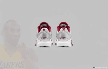 Back view of a pair of sneakers with white and burgundy colors, featuring a signature and a number 33 on the heels. A faded image of a basketball player in a Lakers jersey is in the background.