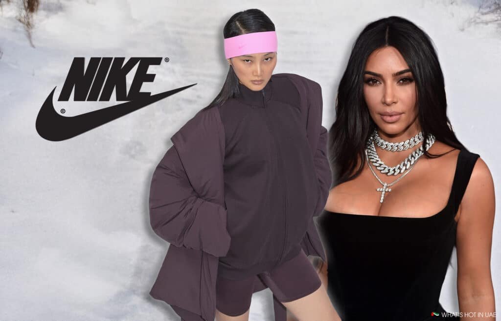 A fashion model wearing a Nike outfit with a pink headband stands next to a woman in a black dress with layered necklaces in front of a snowy background with the Nike logo displayed prominently.