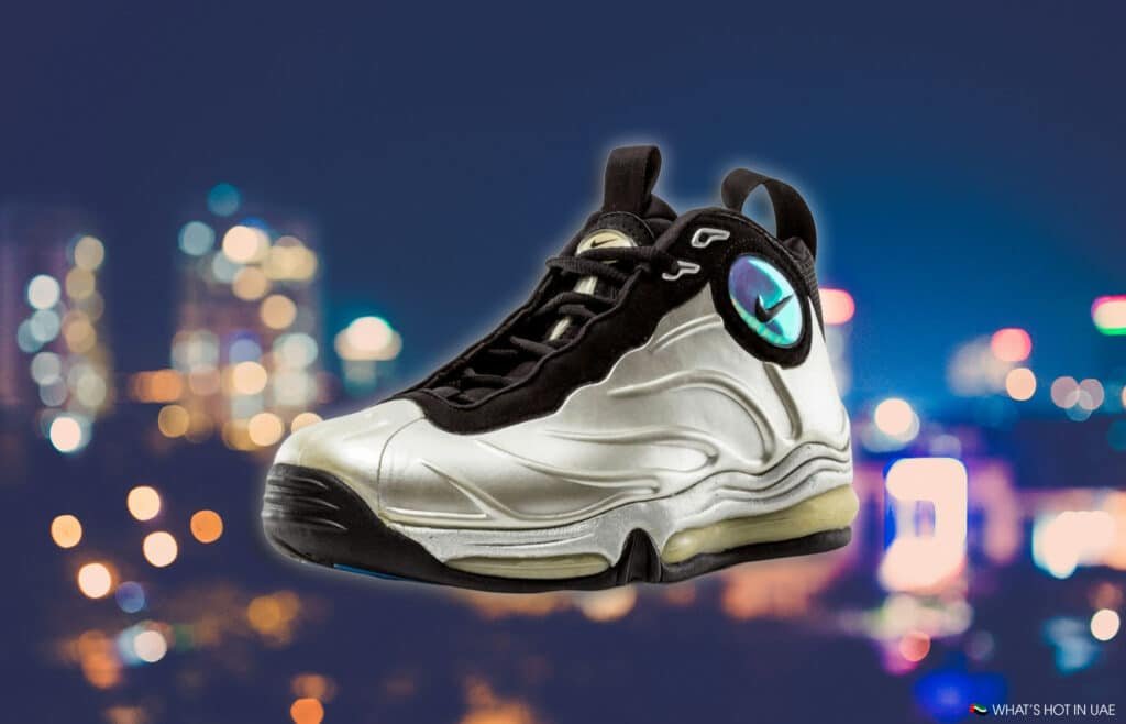 A silver and black sneaker with a prominent reflective design against a blurred cityscape background at night.
