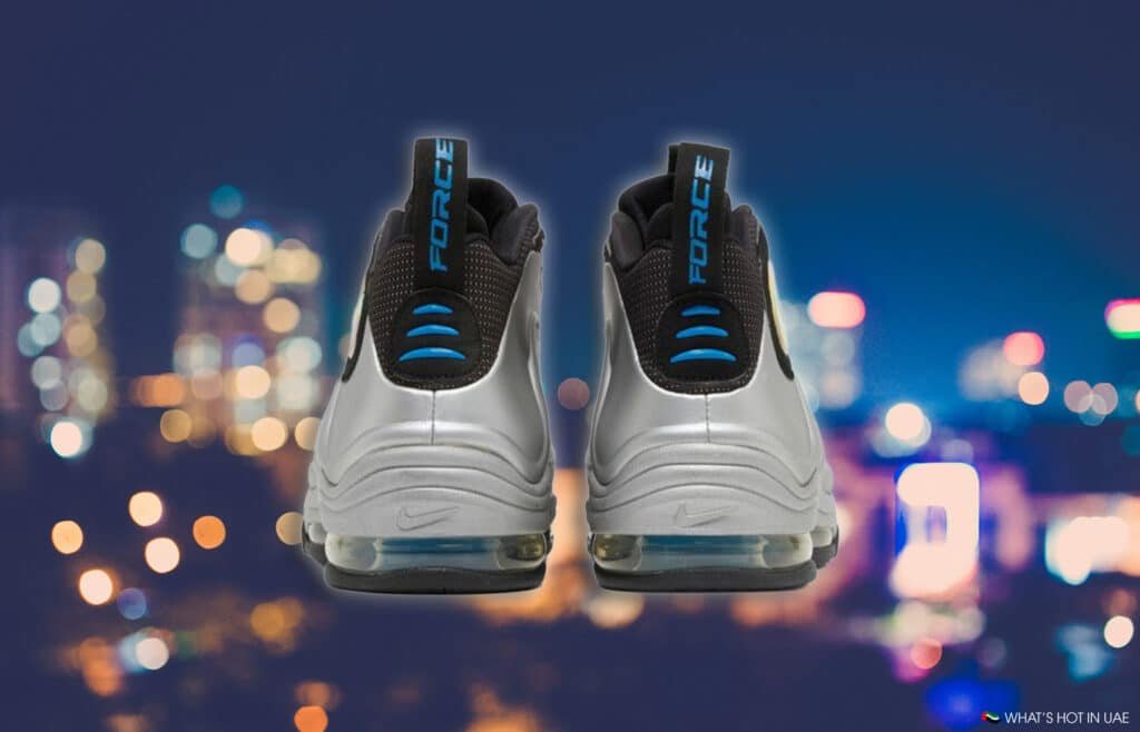 A pair of silver sneakers with black and blue accents displayed against a blurred city lights background.