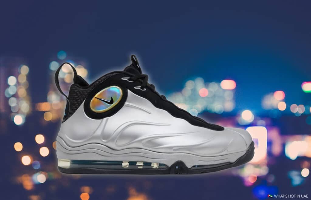 A silver and black Nike sneaker with an iridescent logo on the side, displayed against a blurred city lights background.