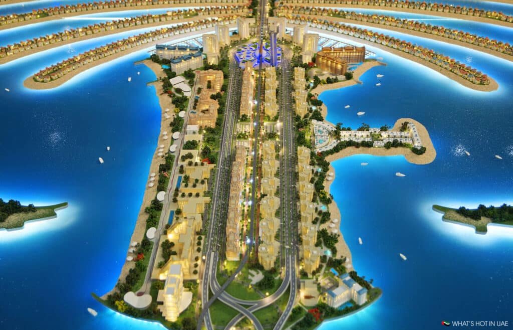 Aerial view of a detailed architectural model depicting a Palm Jumeirah Plot shaped like a palm tree, surrounded by blue water and featuring illuminated buildings, roads, and greenery on each of its fronds.