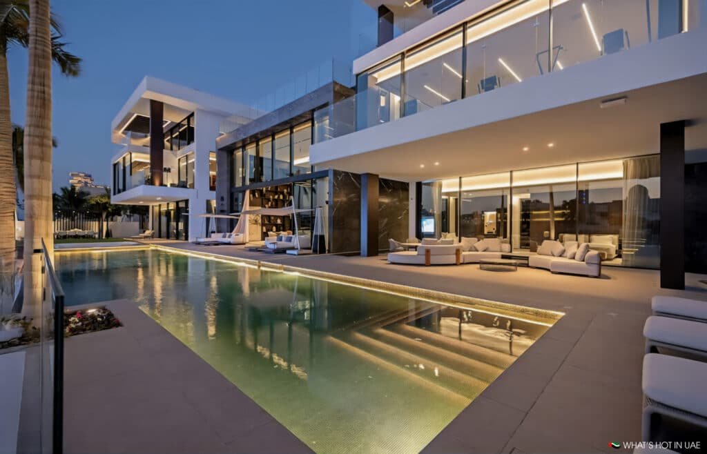 A modern Palm Jumeirah Plot at dusk featuring large glass windows, an illuminated swimming pool, and stylish outdoor seating areas.