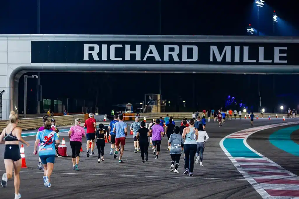 RunYAS 2026: Your Ultimate Guide to Abu Dhabi's New Running Festival at Yas Marina CircuitA group of people jogging on a race track at night, with a large 'RICHARD MILLE' sign overhead.