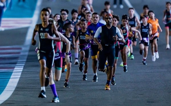 A group of athletes running on a track during a race, with various participants wearing different athletic attire. The setting appears to be a formal race event.