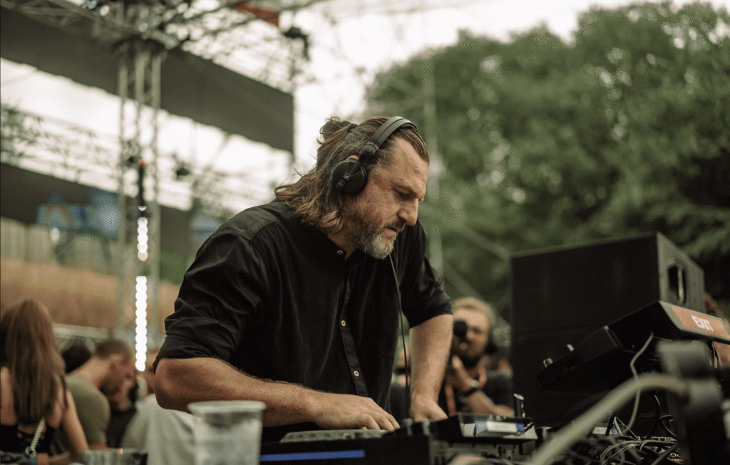 Solomun in Dubai: A person wearing headphones is focused on operating DJ equipment at an outdoor event, surrounded by people and greenery.