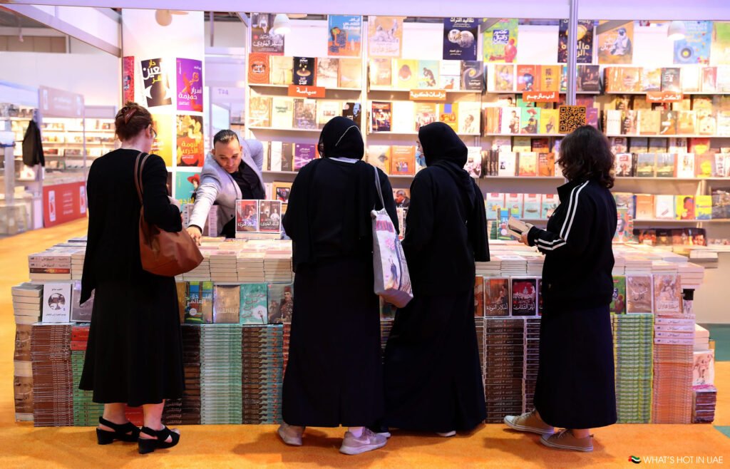 People shopping at a book fair, browsing through books displayed on tables and shelves with a vendor assisting them.