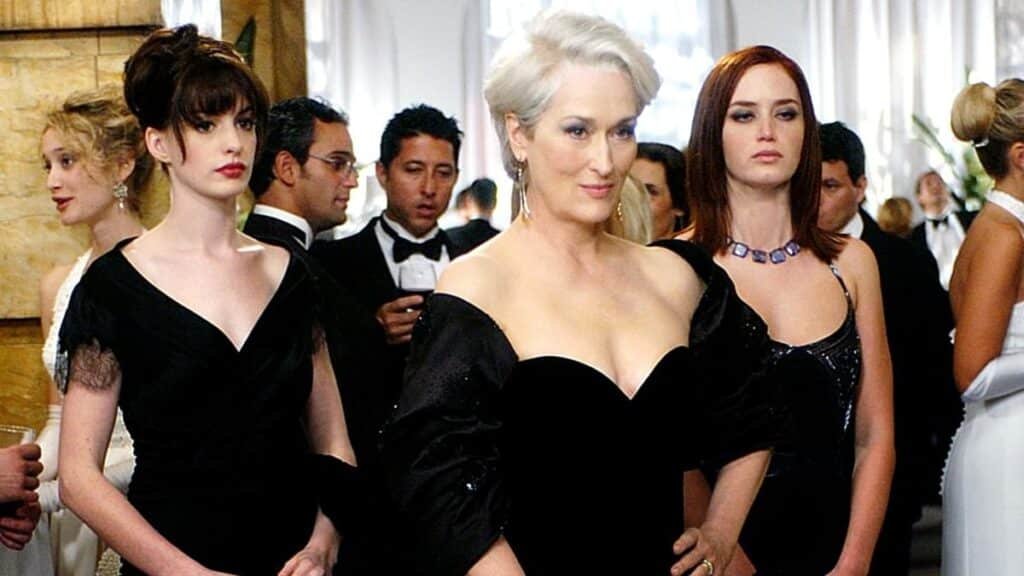 The Devil Wears Prada 2: Three women in elegant black dresses at a formal event, surrounded by other well-dressed guests.