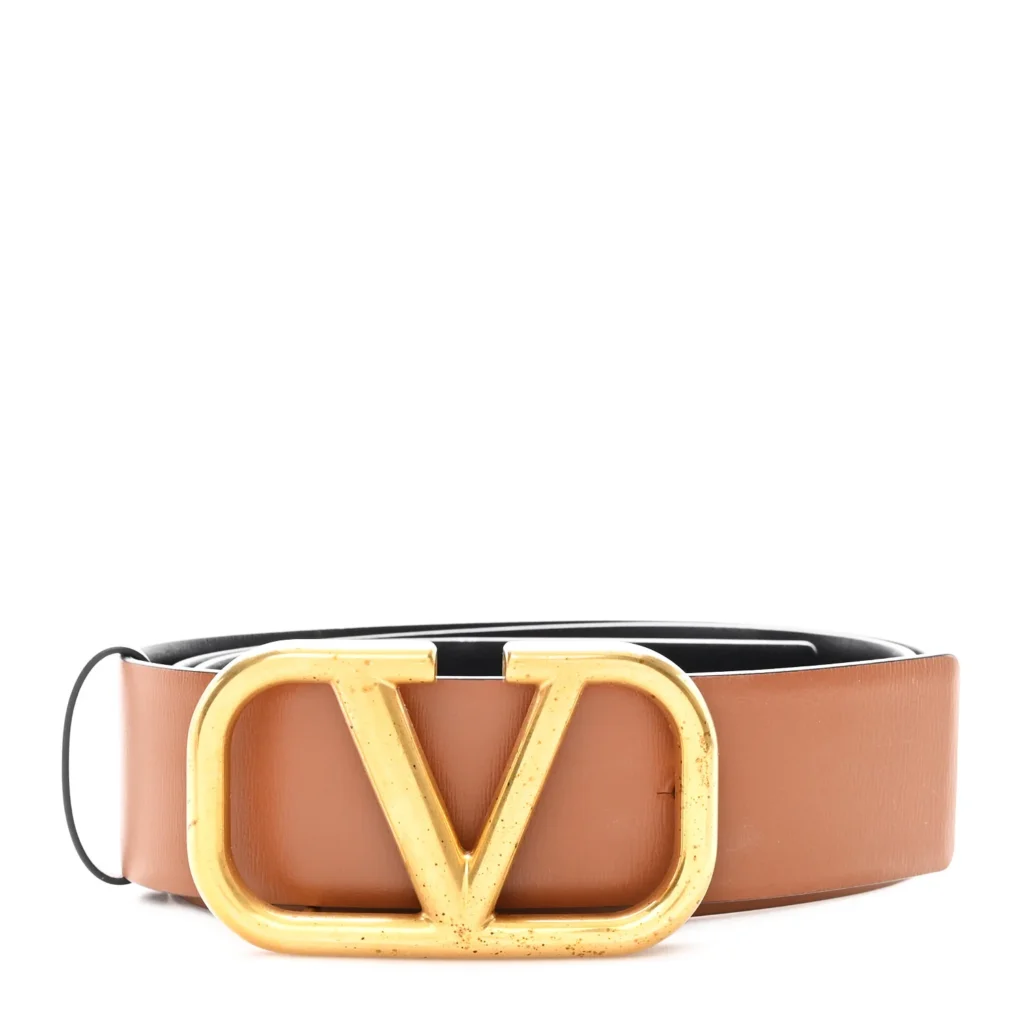 A brown leather belt with a large gold logo buckle in the center.