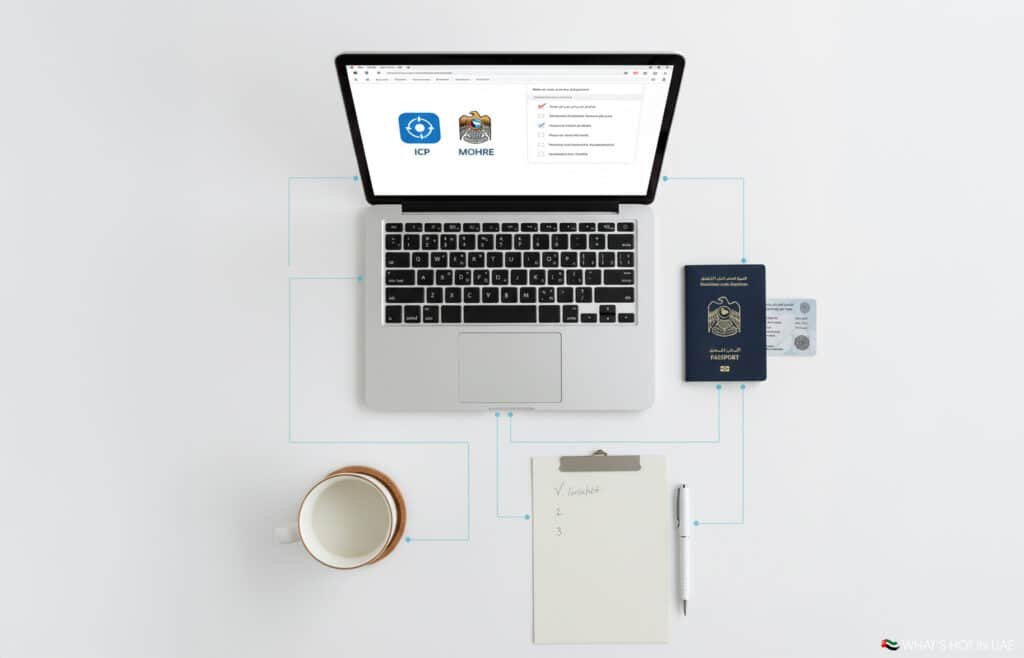 A top-down view of a laptop displaying an online portal, a UAE Freelance Visa passport and ID card, a notepad with a written checklist, a pen, and a coffee mug on a white surface.