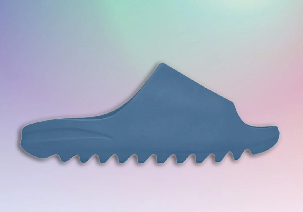 Blue Kanye West Yeezy Slides with a minimalist design and a textured sole, set against a gradient background of soft pastel colors.