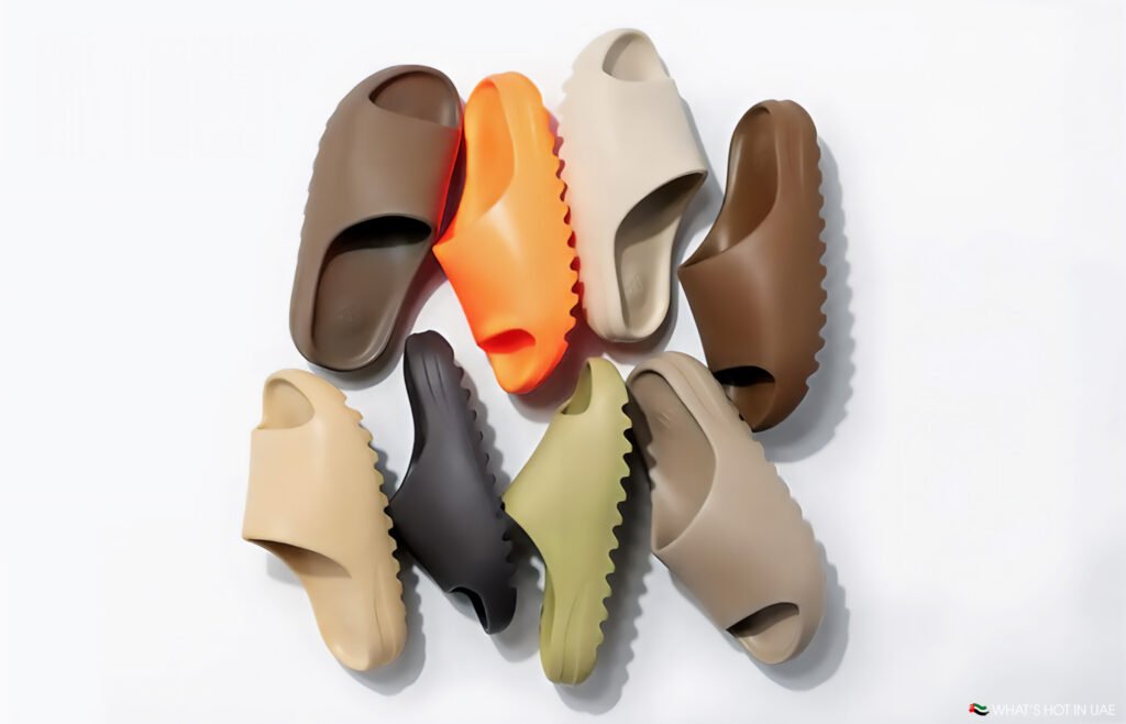 A collection of Kanye West Yeezy Slides in various colors, including brown, beige, orange, and green, arranged in a circular pattern on a white background.
