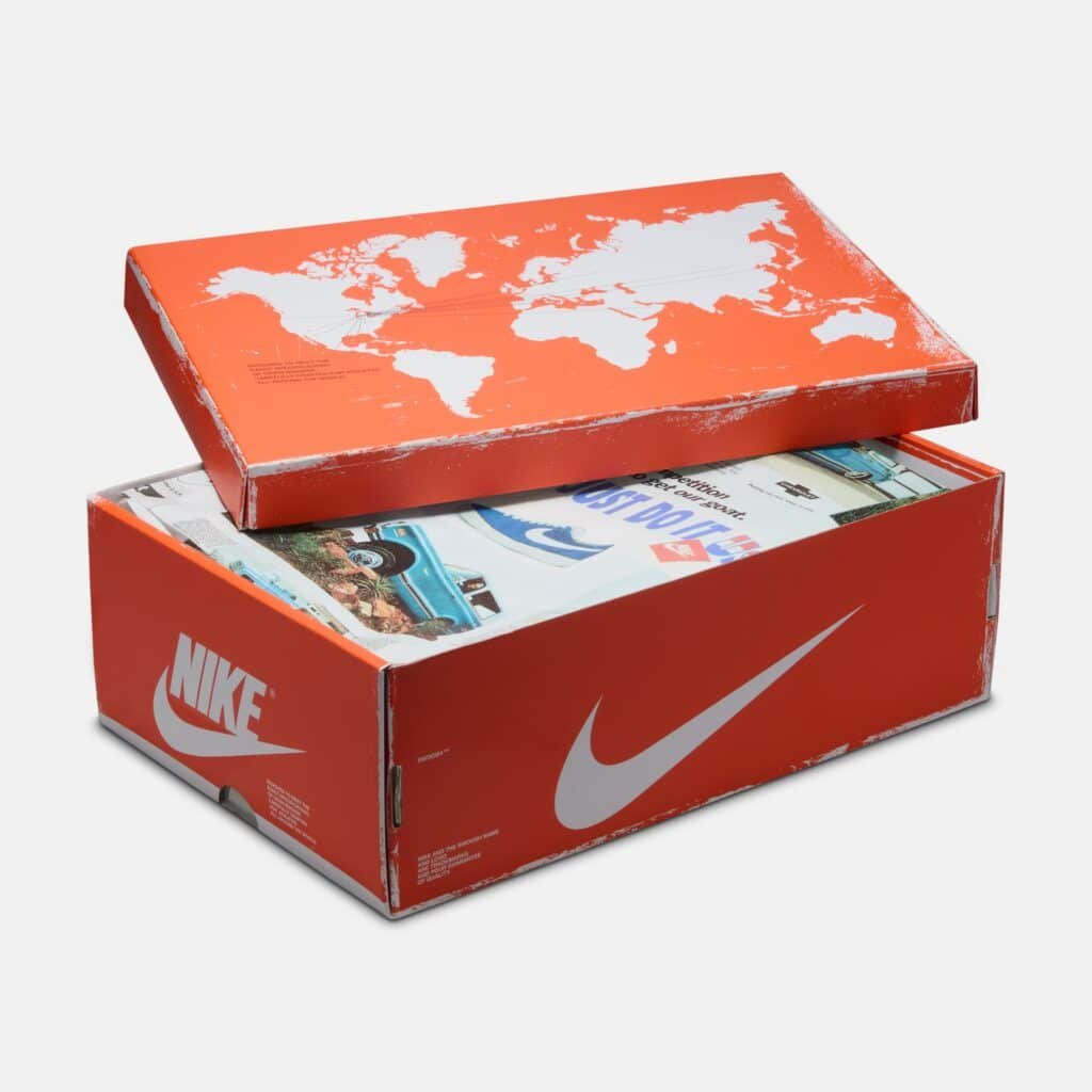 An orange Nike shoe box with a world map design on the lid, partially opened to reveal a colorful printed interior.