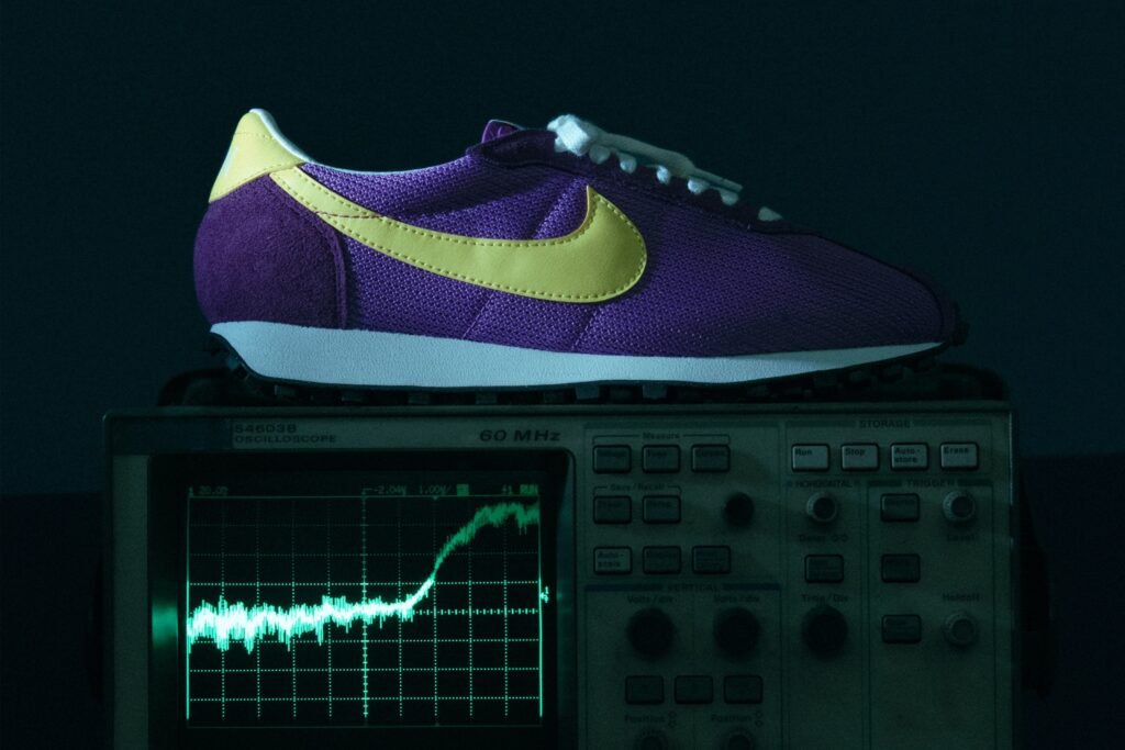 A purple and yellow sneaker rests on top of an oscilloscope displaying a waveform on its screen.