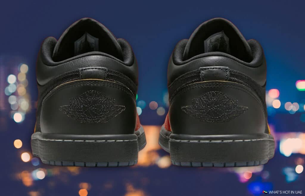 A pair of black Air Jordan 1 Low 'Money Cat' sneakers with an embossed logo on the heel, set against a blurred city nightscape.
