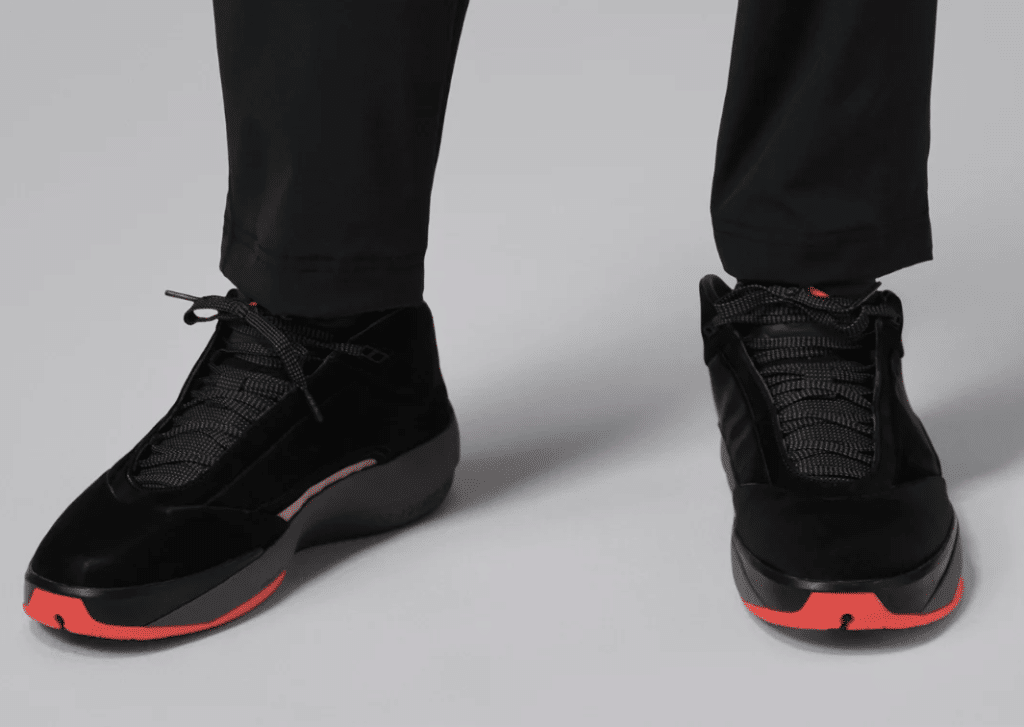 A pair of black Air Jordan 40 'Infrared' sneakers with red accents on the toe and outsole, worn by a person in black pants.