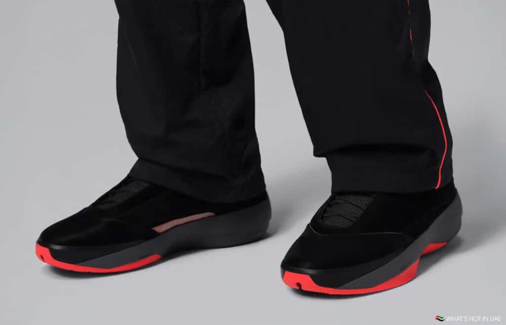 A pair of black shoes with red soles, worn by someone in black pants with red accents.