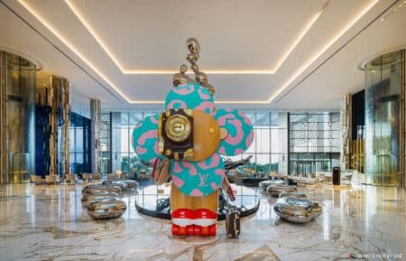 Large, colorful flower-like sculpture with abstract designs displayed in a modern, spacious lobby with sleek decor.
