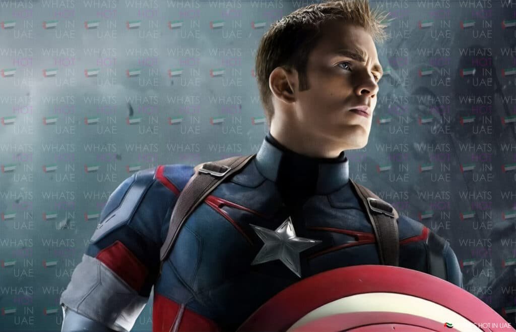 A person in a superhero costume with a star emblem on the chest, holding a shield, set against a backdrop with text.