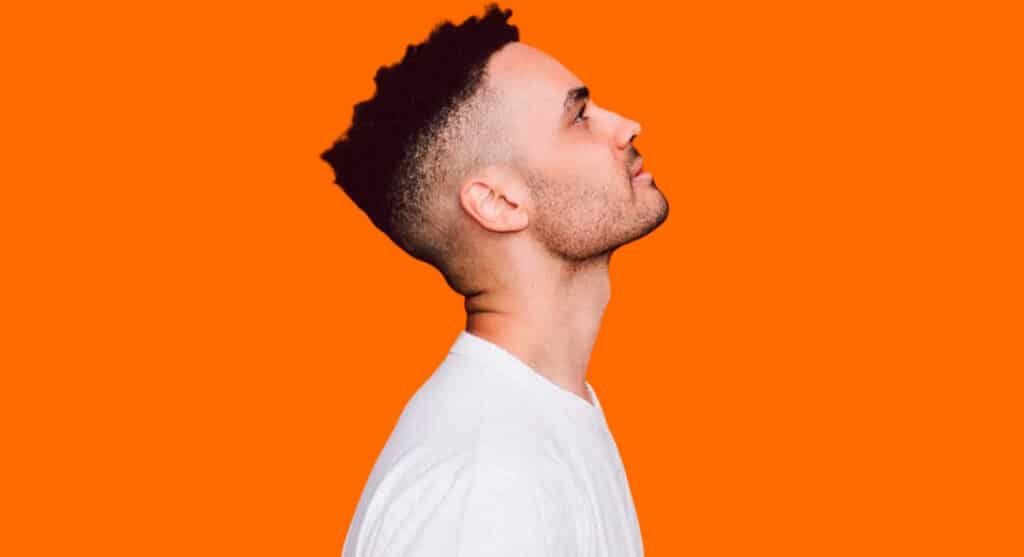 Profile view of a man with a high fade haircut looking upwards against an orange background.
