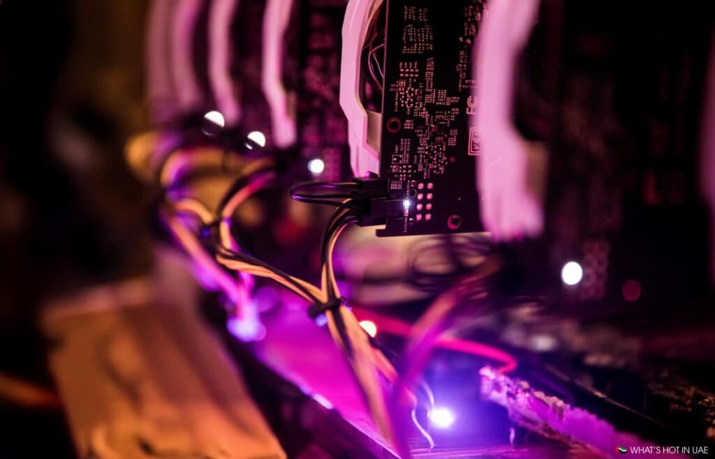Close-up of illuminated computer graphics cards with cables, glowing pink and purple lights in a dark setting.
