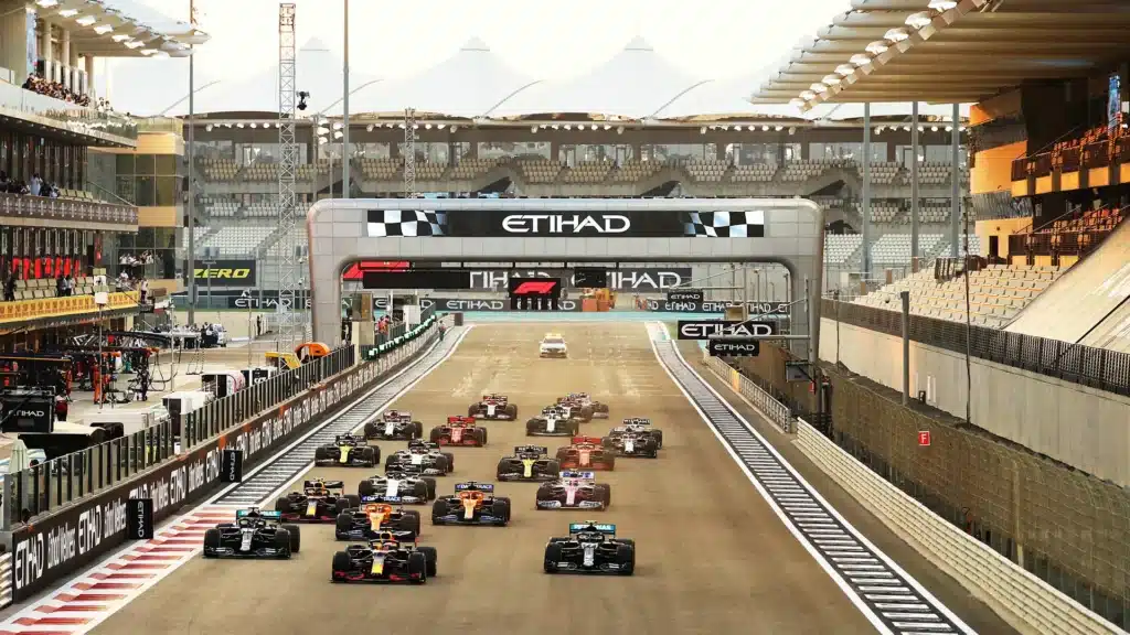 A Formula 1 race in progress at the Yas Marina Circuit, featuring multiple cars on the starting grid with grandstands and a pit lane visible.