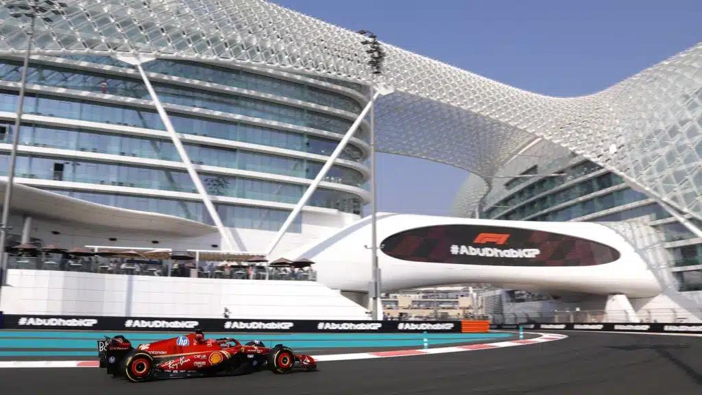 A Formula 1 race car drives on a track in front of the Yas Hotel at the Abu Dhabi Grand Prix, featuring a large F1 and #AbuDhabiGP sign.