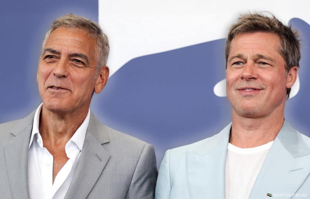 George Clooney & Brad Pitt wearing suits and smiling, standing against a blue and white backdrop.