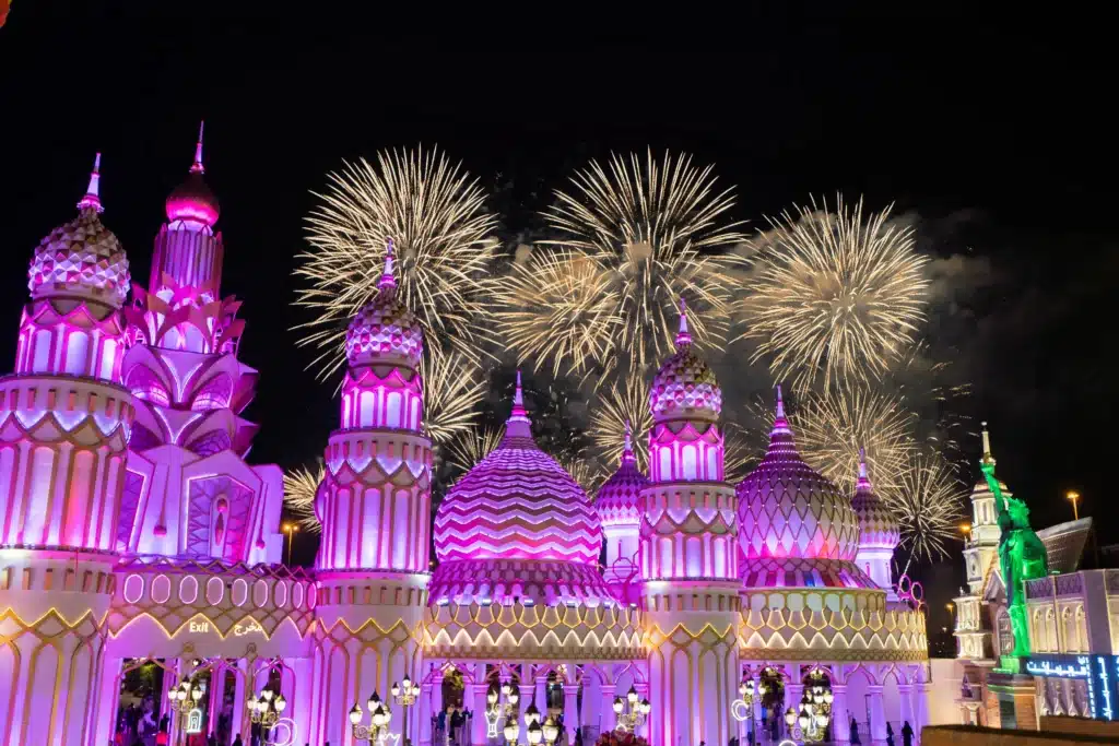 A series of vibrant fireworks light up the night sky above elaborately illuminated, pink and purple domes.