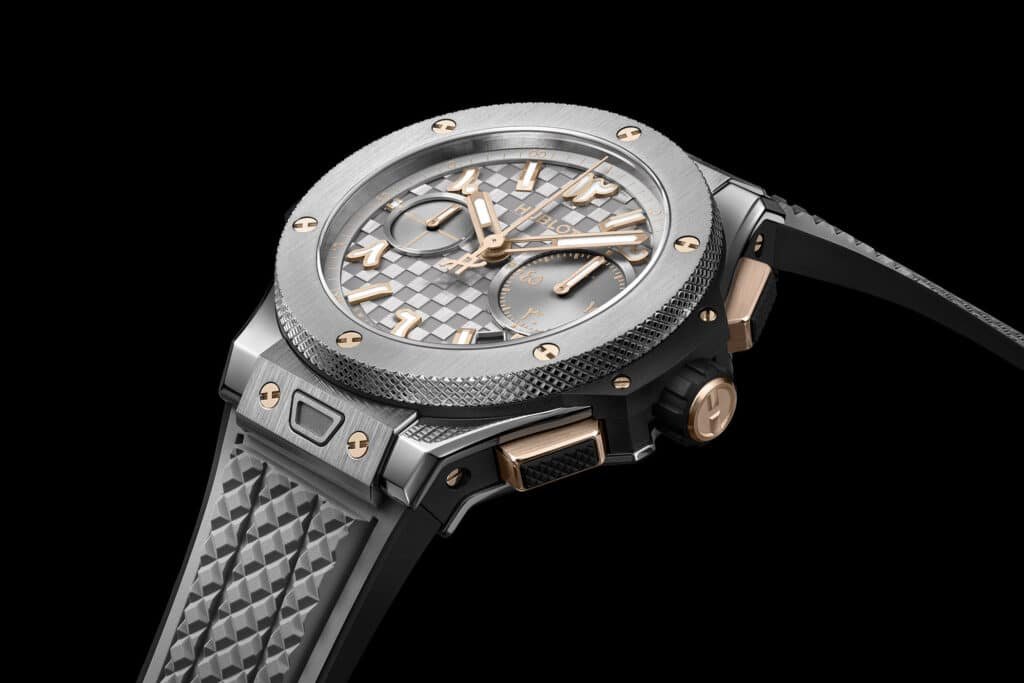 A luxury Hublot Big Bang Dubai watch with a textured grey and silver dial, featuring gold hands and markers, encased in a metal frame with visible screws and a textured black rubber strap.
