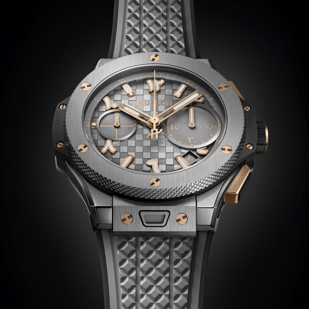 A luxury Hublot Big Bang Dubai watch with a metal bracelet, featuring a textured grey dial with gold accents and Arabic numerals.