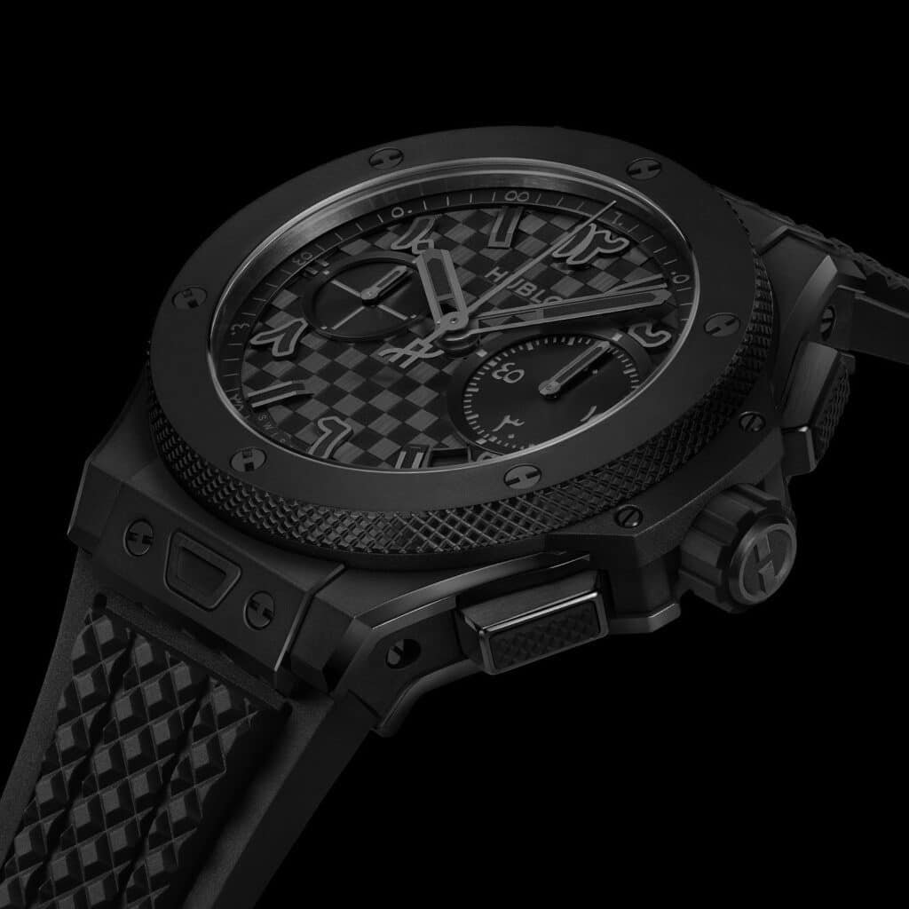 Close-up of a luxury black watch with a textured strap, featuring a checkered dial, bold indices, and multiple sub-dials.