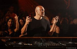 A DJ stands behind a mixing console at a lively nightclub, surrounded by people dancing.