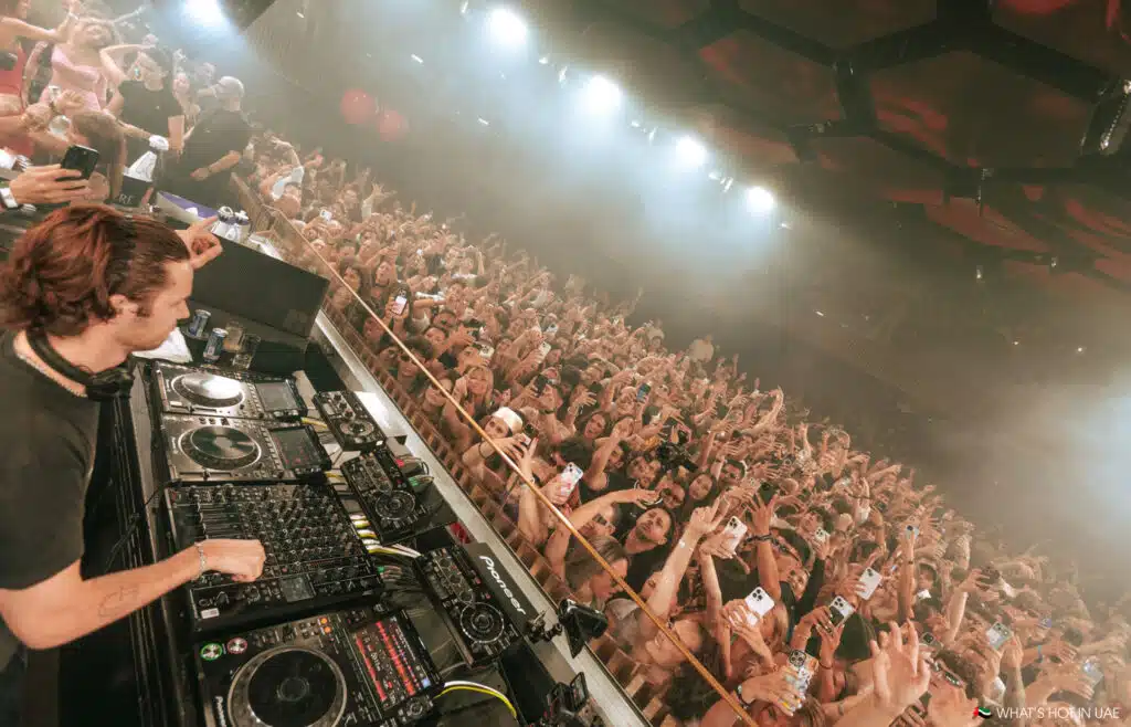 Mau P performs at a lively, crowded Baddest Behavior club night with people dancing and taking photos.
