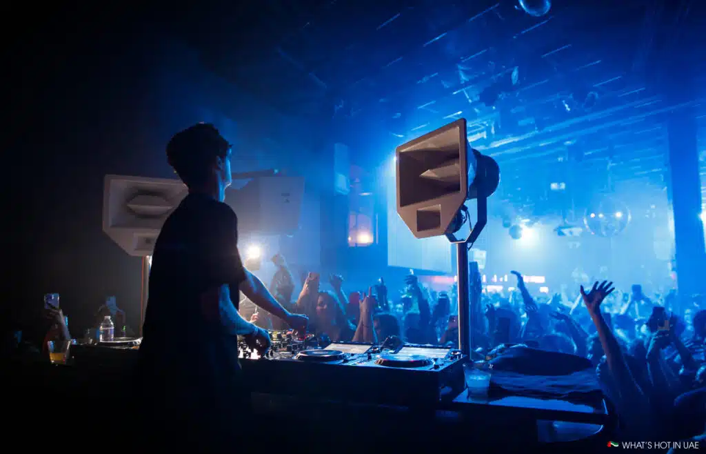 Mau P performing on stage with a crowd dancing under blue lights in a nightclub.