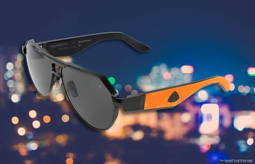 Stylish MAYBACH Eyewear sunglasses with orange and black frames and dark lenses, showcased against a blurred city lights background.