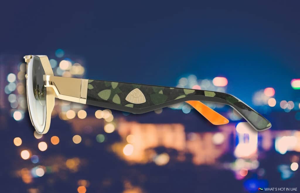 A stylish pair of MAYBACH Eyewear sunglasses with gold accents and a camo-patterned frame, set against a blurred city nightscape.