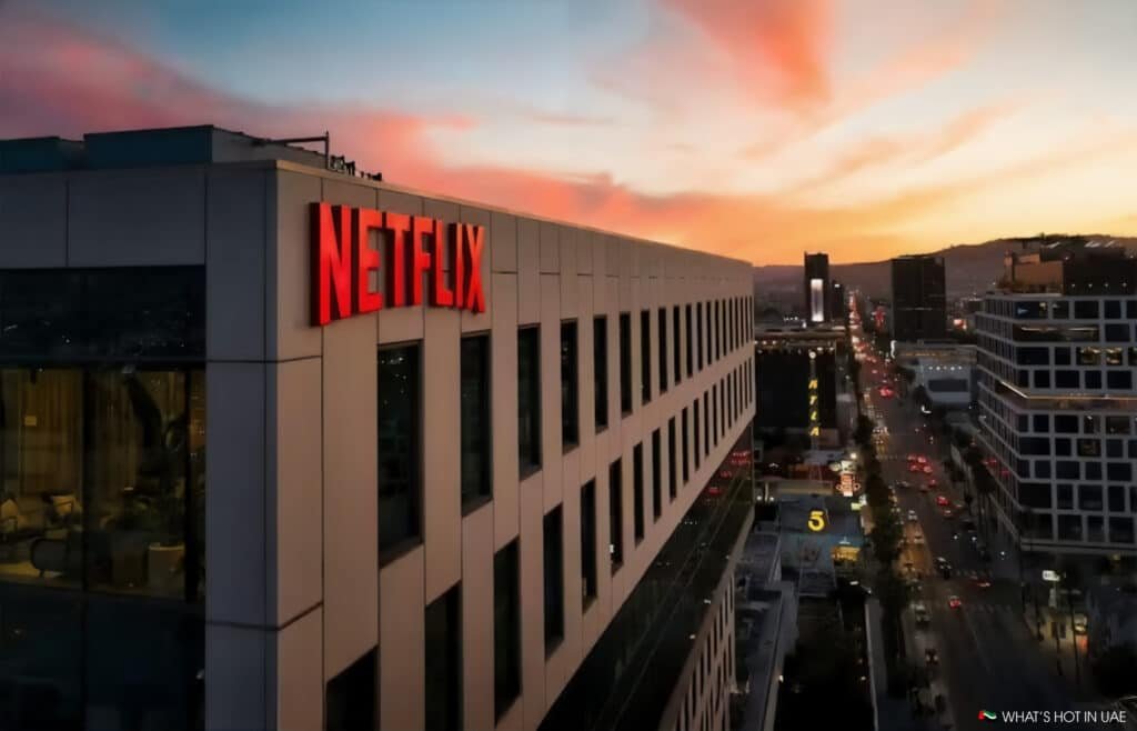 A cityscape at sunset with the Netflix headquarters prominently displaying its red logo, and a bustling street with cars below.