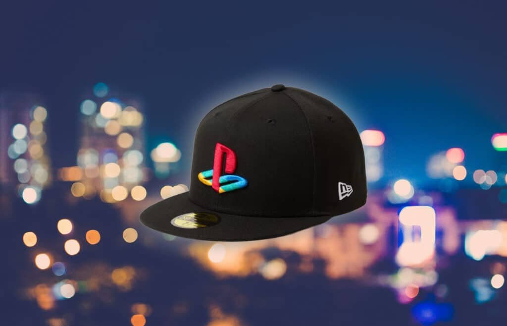 A black New Era x PlayStation Collection cap with a colorful, embroidered logo and a cityscape with blurred lights in the background.