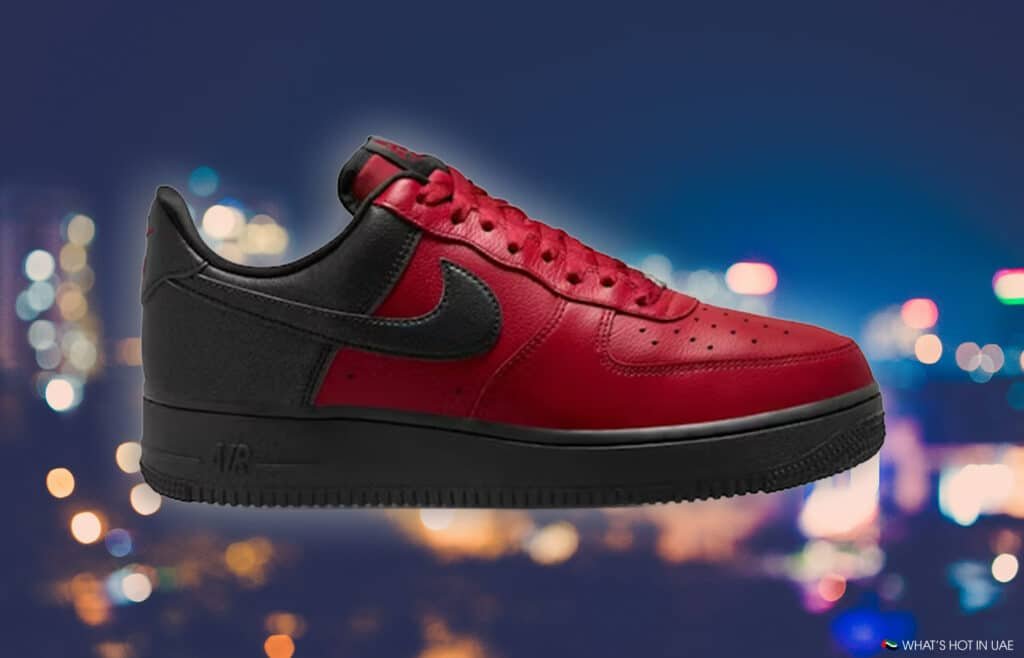 A red and black Nike Air Force 1 Low 'Scarface' sneaker with a swoosh logo, set against a blurred city lights background.