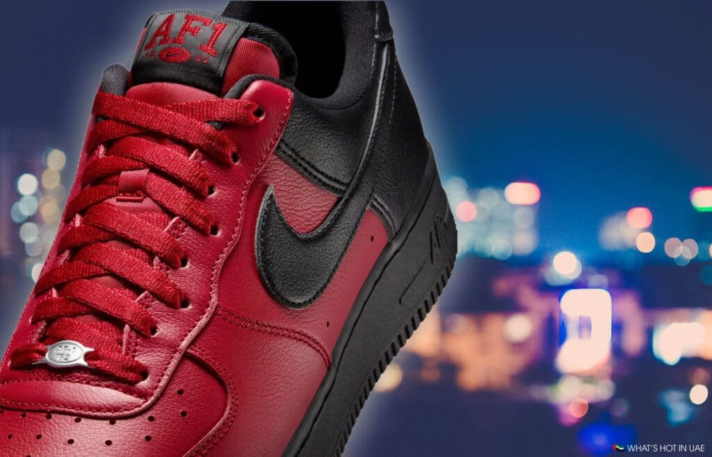 A red and black Nike Air Force 1 Low 'Scarface' sneaker with a Nike logo is shown against a blurred cityscape at night.